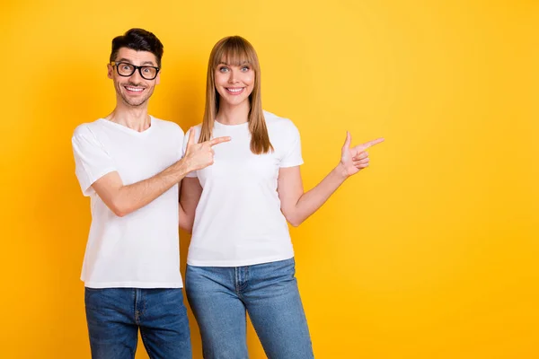 Beyaz t-shirt gözlüklü iki sevimli insanın boş bir yeri işaret ettiği fotoğraf izole edilmiş sarı arka plan — Stok fotoğraf