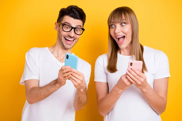 Foto de impactados funky dos personas vestidas de blanco gafas de camiseta que muestran dispositivos modernos boca abierta aislado color amarillo fondo —  Fotos de Stock