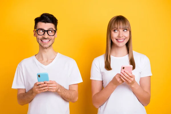 Foto de lindo dulce dos personas vestidas gafas de camiseta que sostienen dispositivos modernos que se miran el uno al otro aislado de color amarillo de fondo —  Fotos de Stock