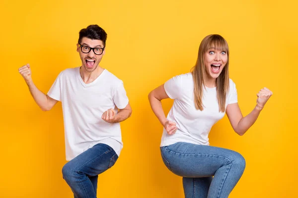 Foto de impressionado sorte duas pessoas vestidas branco t-shirt óculos boca aberta levantando punhos isolado cor amarela fundo — Fotografia de Stock