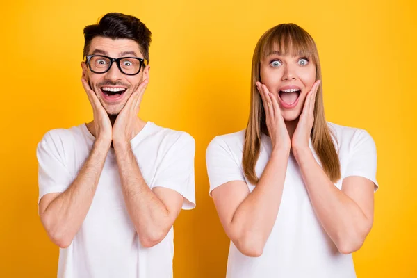 Foto de divertido impresionado dos personas vestidas blanco camiseta gafas boca abierta brazos mejillas aislado color amarillo fondo — Foto de Stock