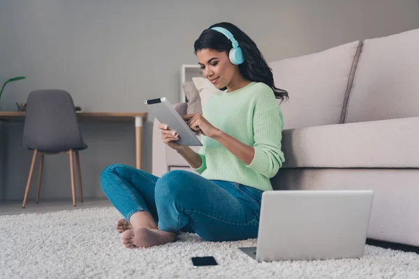 Foto de tamaño completo de afroamericana encantadora mujer joven sentarse uso de suelo portátil usar auriculares dentro de casa — Foto de Stock