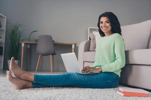 Повна фотографія профілю тіла афро-американської леді сидить підлогу робота ноутбука посмішка ноутбука одягнена в зеленого м'ясника всередині будинку. — стокове фото
