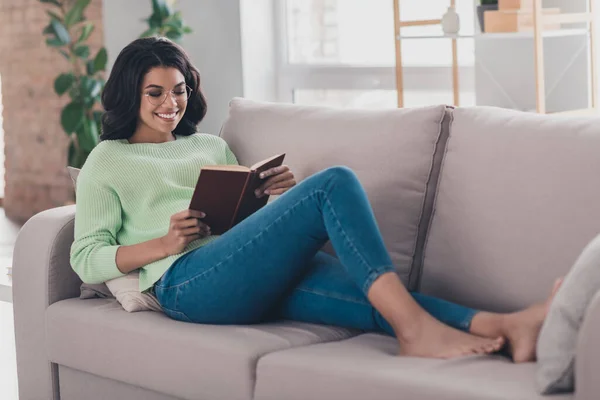 Foto de perfil de tamaño completo de encantadora chica de piel oscura tumbada en el sofá celebrar libro sonrisa dentada fin de semana en casa en interiores — Foto de Stock