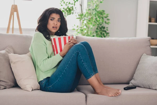 Profilo completo del corpo foto laterale di pelle scura giovane donna sedersi divano spaventato guardare film horror mangiare pop corn al chiuso in casa — Foto Stock