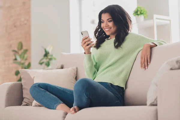 Low angle view full body photo of young woman happy positive smile look read browse cellphone sit sofa home — Stockfoto
