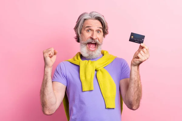 Retrato de atractivo hombre de pelo gris alegre sosteniendo en tarjeta bancaria de la mano celebrando divertirse aislado sobre fondo de color pastel rosa — Foto de Stock