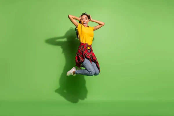 Full längd foto av funky upphetsad mörk hud kvinna bära gul t-shirt hoppa armar huvud isolerad grön färg bakgrund — Stockfoto