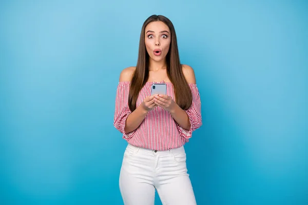 Portret van aantrekkelijke verbaasd recht-harig meisje met behulp van cel lezen nieuws geïsoleerd over helder blauwe kleur achtergrond — Stockfoto