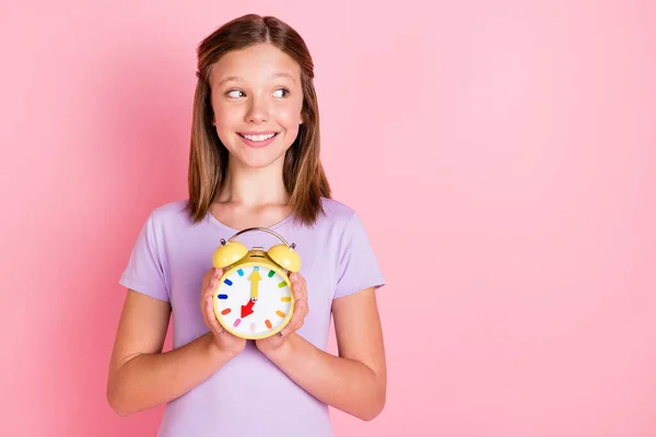 Foto de alegre positivo olhar menina pequena stand espaço vazio segurar mãos relógio isolado no fundo cor-de-rosa — Fotografia de Stock