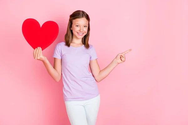 Foto de feliz bonito menina ponto dedo vazio espaço mantenha grande coração vermelho isolado no fundo cor-de-rosa pastel — Fotografia de Stock