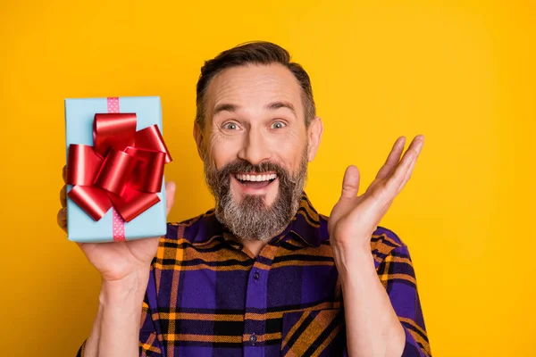 Foto retrato de hombre sonriente feliz mostrando regalo envuelto en fiesta de cumpleaños sorprendido aislado en el fondo de color amarillo vibrante —  Fotos de Stock