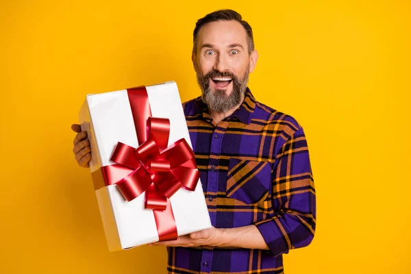 Foto de sorprendido emocionado hombre maduro feliz celebrar regalo caja de vacaciones presente aislado sobre fondo de color amarillo brillante —  Fotos de Stock