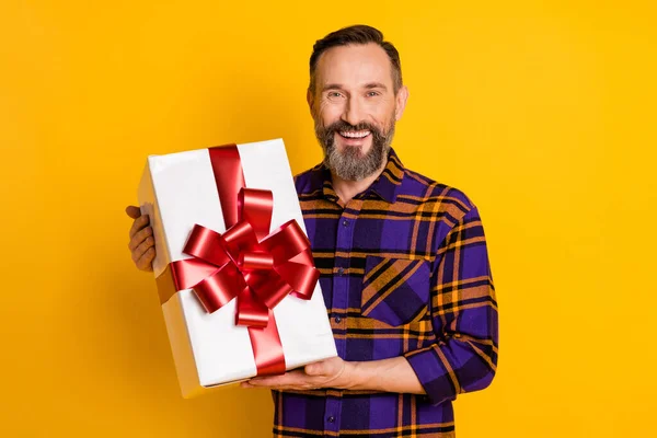 Retrato de cara alegre atraente vestindo camiseta verificada segurando em mãos arco caixa de fita isolada sobre fundo de cor amarelo brilhante — Fotografia de Stock