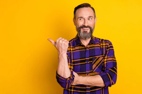 Портрет привлекательного веселого парня в клетчатой рубашке, показывающий пространство для копирования, изолированное на ярко-желтом фоне — стоковое фото