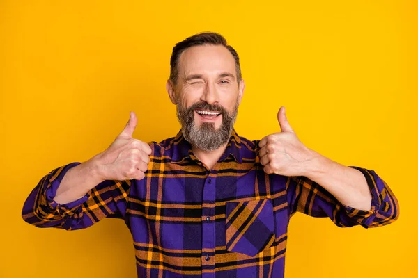 Portrait of attractive cheerful guy wearing checked shirt showing double thumbup winking ad isolated over bright yellow color background — Stock Photo, Image