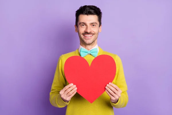 Portrét brunet optimistický chlap držet papír srdce nosit žlutý svetr izolované na pastelové šeříkové barvy pozadí — Stock fotografie