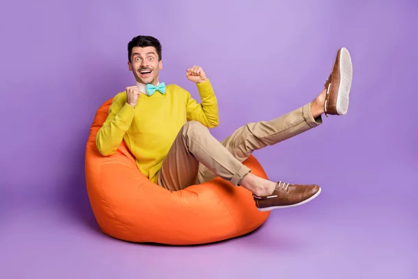 Full size foto di bruno hooray ragazzo sedersi su borsa usura giallo maglione pantaloni scarpe da ginnastica isolato su sfondo color lilla pastello — Foto Stock