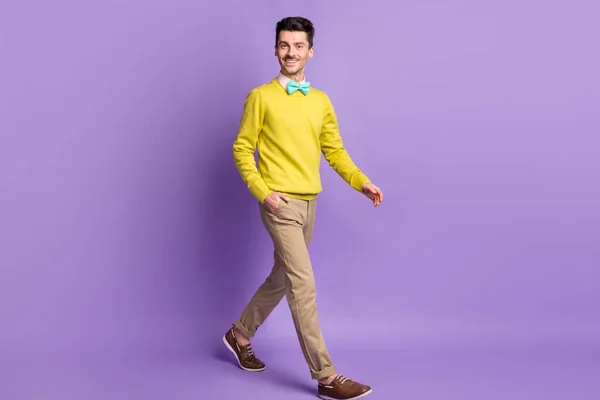 Full size profile photo of brunet optimistic guy go hand in pockets wear yellow sweater trousers sneakers isolated on lilac background — Stock Photo, Image