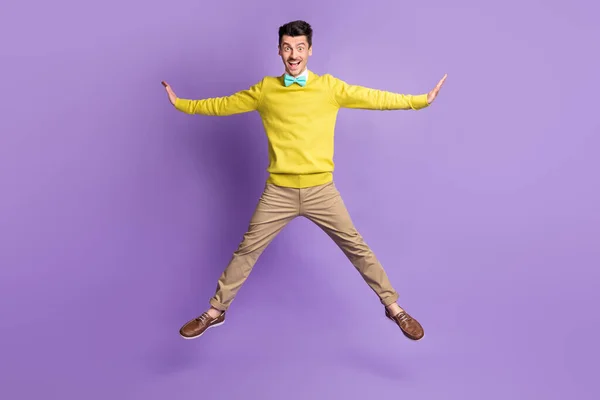 フルサイズ写真のブルネット楽観的な男ジャンプ着用黄色セーターパンツスニーカー絶縁でライラック背景 — ストック写真