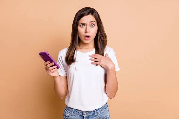 Foto retrato de mujer joven malentendido despistado celebración de teléfono celular aislado pastel color beige fondo — Foto de Stock