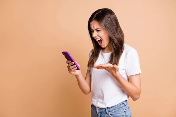Foto retrato de chica furiosa loca gritando manteniendo el teléfono celular enojado loco aislado pastel beige color fondo —  Fotos de Stock