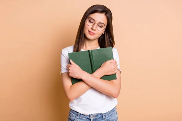 Retrato fotográfico de una estudiante de ensueño con gafas que abraza el libro preparándose para la prueba de fondo de color beige pastel aislado —  Fotos de Stock