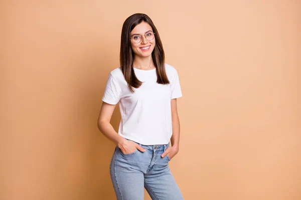 Фотопортрет студентки в очках, улыбающейся в белых джинсах с футболками, на фоне пастельно-бежевого цвета — стоковое фото