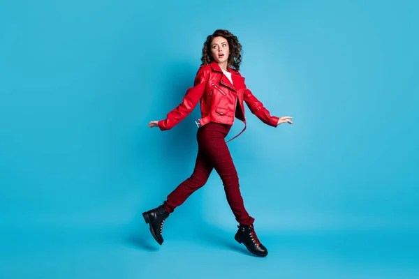 Foto de perfil de tamaño completo de la chica linda impresionada salto desgaste chaqueta roja pantalones botas aisladas sobre fondo de color azul — Foto de Stock