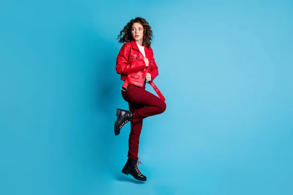 Full size profile photo of impressed girl jump look back wear red jacket trousers boots isolated on blue background — Stock Photo, Image