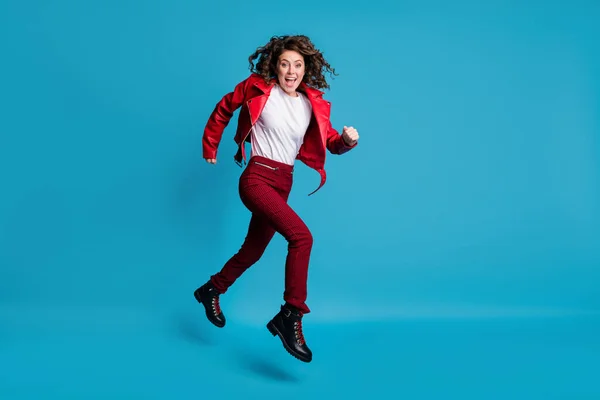 Foto de perfil de tamaño completo de la niña hooray salto correr desgaste chaqueta roja pantalones botas aisladas sobre fondo azul — Foto de Stock