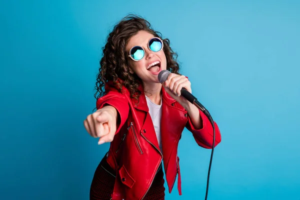 Photo of crazy carefree lady open mouth sing hold mic direct finger on you wear round sunglass isolated on blue color background — Stock Photo, Image