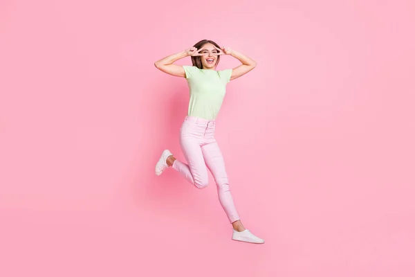 Портрет чарівної дівчини, що стрибає на високому показі, дві руки пальці v-знак біля очей ізольовані на фоні рожевого кольору — стокове фото