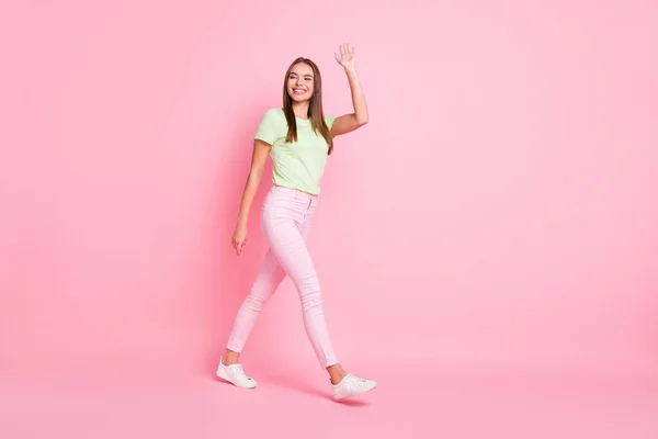 Volledige lengte foto van schattig mooi jong meisje gekleed groen t-shirt lopen zwaaien arm bye geïsoleerde pastel roze kleur achtergrond — Stockfoto