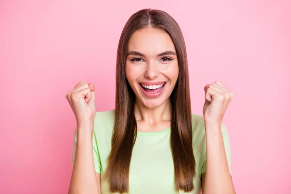 Foto de divertida chica afortunada vestida camiseta verde levantando puños aislados pastel color rosa fondo — Foto de Stock