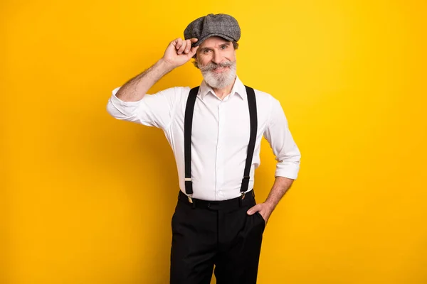 Foto de hombre maduro feliz sonrisa positiva mano tacto retro sombrero tirantes aislados sobre fondo de color amarillo —  Fotos de Stock