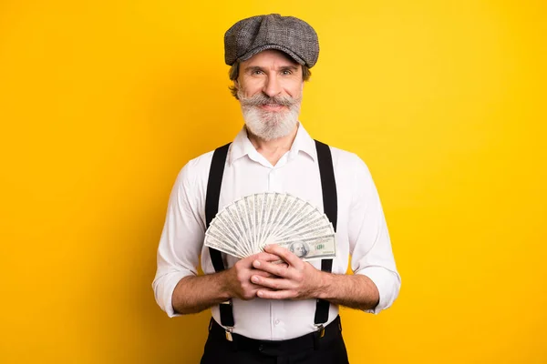 Mutlu mutlu gülümseyen yaşlı adamın fotoğrafı. Para içinde yüzlercesi var. Sarı arka planda izole edilmiş. — Stok fotoğraf