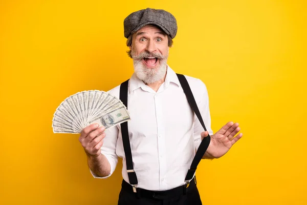 Photo of aged man happy positive smile excited hold money dollars hundreds wealthy isolated over yellow color background — Stock Photo, Image