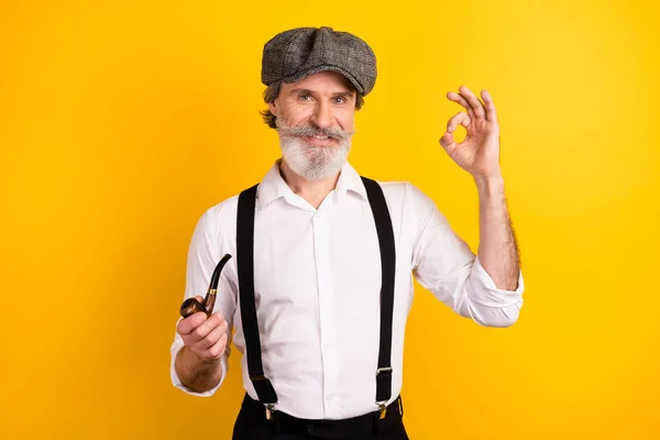 Foto porträtt av gentleman i skjorta hängslen hålla trä röret visar ok tecken isolerad levande gul färg bakgrund — Stockfoto