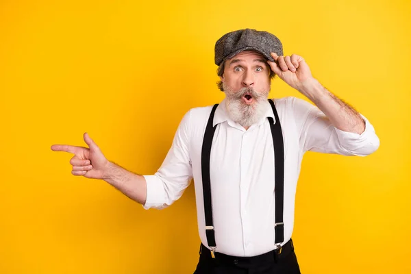 Foto retrato de homem barbudo na camisa surpreendente tocando cap apontando copyspace isolado cor amarela brilhante fundo — Fotografia de Stock