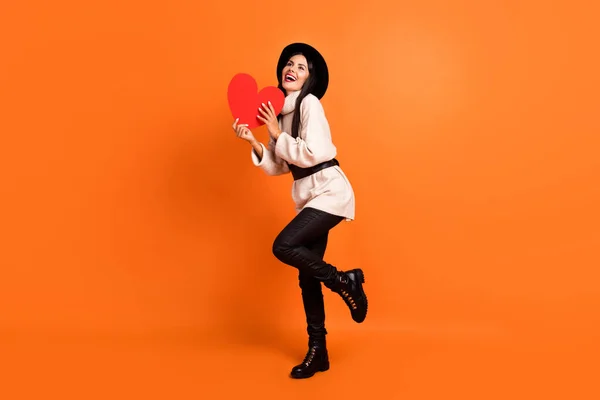 Foto de tamaño completo de joven encantadora chica sonriente encantadora mirada copyspace mantener el corazón de papel rojo aislado sobre fondo de color naranja —  Fotos de Stock