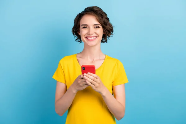 Foto van mooie vrolijke meisje houden telefoon look camera dragen geel t-shirt geïsoleerde blauwe kleur achtergrond — Stockfoto