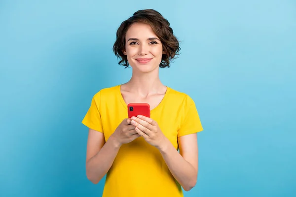 스마트폰을 들고 있는 아주 긍정적 인 젊은 여성의 사진 노란색 티셔츠 고립된 푸른 색 배경을 띠고 있다 — 스톡 사진
