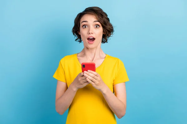 写真のかわいい驚きの女の子ホールド携帯電話オープン口を着用黄色tシャツ隔離された青の色の背景 — ストック写真