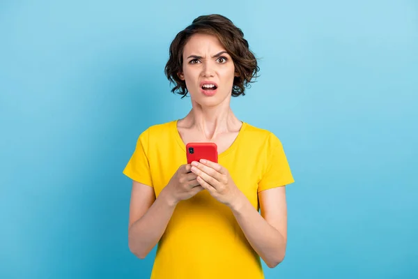 Foto van verbaasd jong meisje houden smartphone sprakeloos walgelijke slijtage geel t-shirt geïsoleerde blauwe kleur achtergrond — Stockfoto