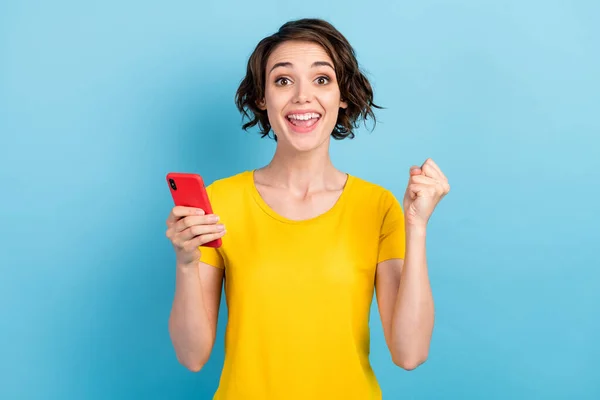 Foto de menina surpreendida segurar telefone boca aberta levantar punho louco rosto desgaste amarelo t-shirt isolado azul cor fundo — Fotografia de Stock