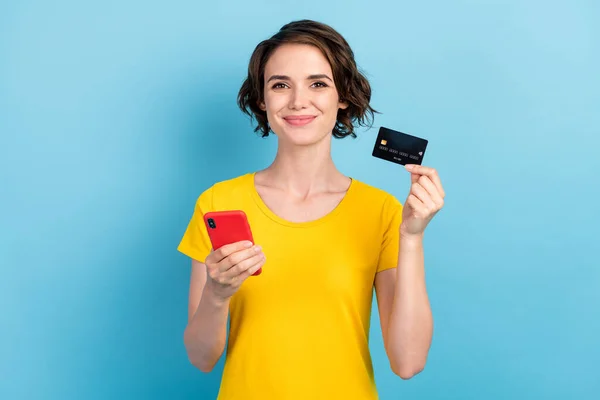 Fénykép vidám csinos hölgy tartsa telefon hitelkártya viselni sárga póló elszigetelt kék szín háttér — Stock Fotó