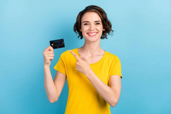 Фотографія позитивної дівчини, що тримає пластикову кредитну картку, вказує на те, що палець носить жовту футболку ізольований синій колір фону — стокове фото