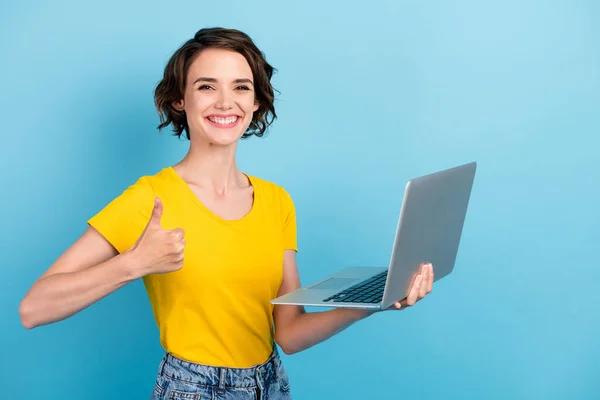 Φωτογραφία του γοητευτικό κορίτσι κρατήσει φορητό υπολογιστή ακτινοβολούν χαμόγελο αυξήσει τον αντίχειρα-up φορούν κίτρινο t-shirt απομονωμένο φόντο μπλε χρώμα — Φωτογραφία Αρχείου