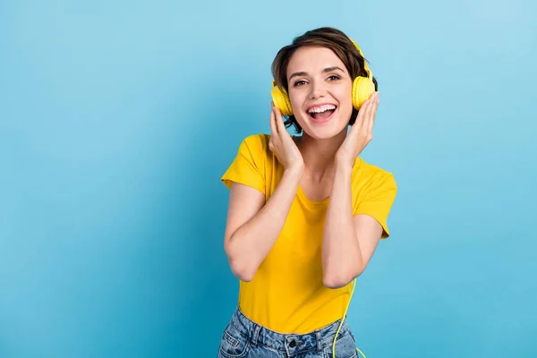 Foto de chica joven encantadora escuchar música boca abierta mirar cámara usar auriculares camiseta amarilla aislado color azul fondo —  Fotos de Stock